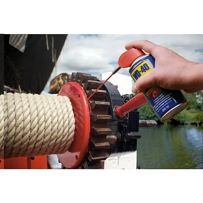 WD-40 Lubricante Doble Acción - 250 ml - Una mano rocía WD-40 sobre una rueda dentada. El producto multiusos es ideal para el mantenimiento de piezas móviles de máquinas.