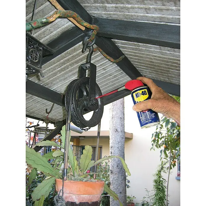 WD-40 Lubricante Doble Acción - 250 ml - Se está utilizando WD-40 para lubricar una polea negra que cuelga de un gancho debajo de una estructura de jardín, lo que facilita la jardinería.