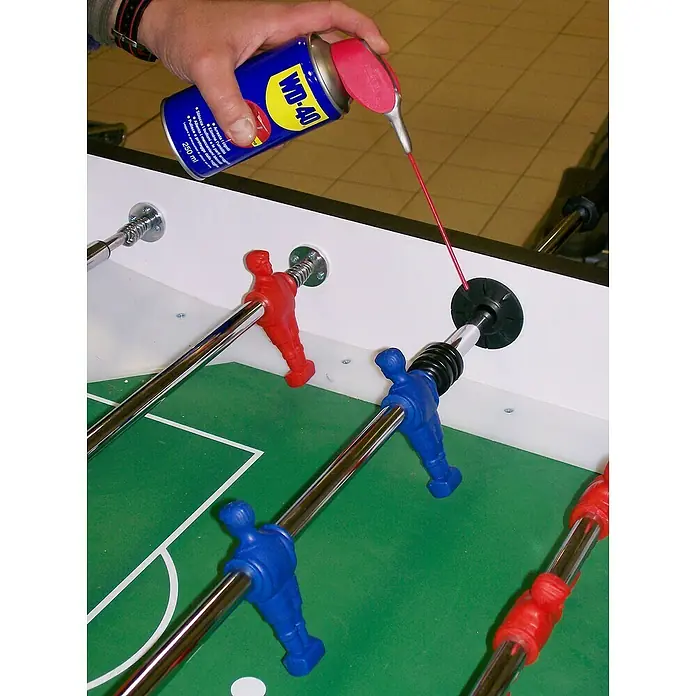 WD-40 Lubricante Doble Acción - 250 ml - Lubricando una mesa de futbolín con WD-40, asegurando movimientos suaves y prolongando la vida útil del juego.