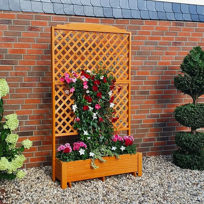 Promadino Pflanzkasten Romantica - Außenmaß (L x B x H): 120 x 38 x 210 cm, Holz, Honigbraun - Ein hölzernes Pflanzgefäß mit Rankgitter, bepflanzt mit bunten Blumen, steht vor einer Ziegelmauer. Ideal für Garten und Terrasse.