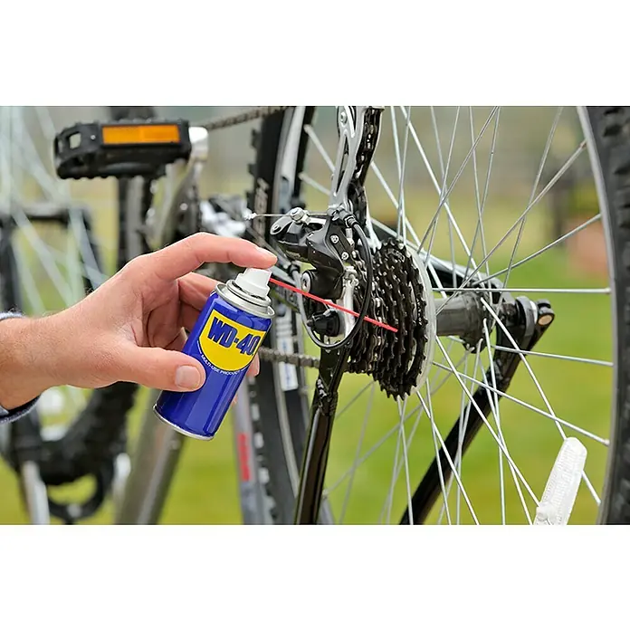 WD-40 Aceite para herrajes multiuso - 100 ml - Primer plano de un hombre rociando WD-40 Producto multiusos en el cassette de una bicicleta para lubricarlo y protegerlo del óxido.