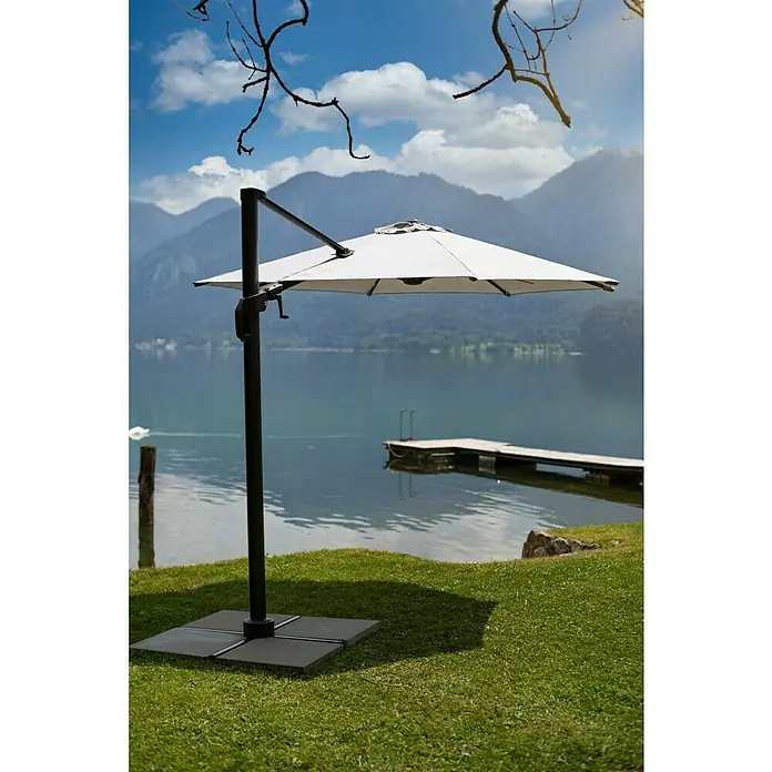 Sunfun Ersatz-Bezug Monaco - Hellgrau, Passend für: Sunfun Ampelschirmgestell Monaco Ø 300 cm - Ein eleganter, quadratischer Sonnenschirm in Weiß steht auf einem grünen Rasen mit einem malerischen See und Bergen im Hintergrund.