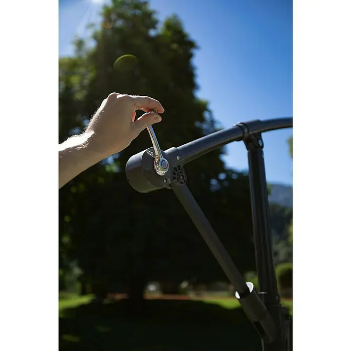 Sunfun Ampelschirm Toscana - Anthrazit, Durchmesser Bespannung: 300 cm - Eine Hand betätigt die Kurbel eines Sonnenschirms, um ihn zu öffnen oder zu schließen. Das Gestell ist aus dunklem Metall.