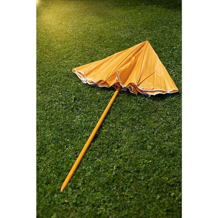 Sunfun Strandschirm - Gelb/Orange, Durchmesser Bespannung: 180 cm - Ein gelber Sonnenschirm liegt auf einer grünen Rasenfläche und bietet einen Farbtupfer in der Natur. Der Schirm ist geschlossen und bereit für seinen nächsten Einsatz.