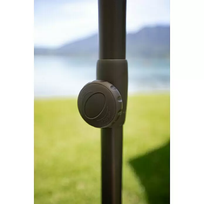 Sunfun Marktschirm rund Torino - Natur, Durchmesser Bespannung: 270 cm - Dunkelgrauer Kunststoff-Verriegelungsknopf an einer Stange mit „LOCK“- und „UNLOCK“-Beschriftung, vor verschwommener See- und Bergkulisse.