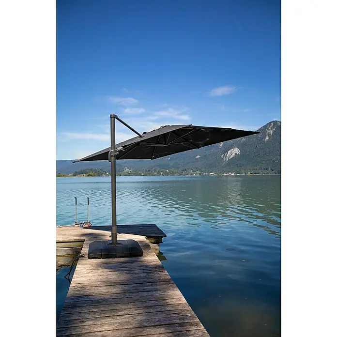 Sunfun Ampelschirm Capri - Anthrazit, Bespannungsmaß (L x B): 300 x 350 cm - Ein großer, quadratischer Sonnenschirm steht auf einem Holzsteg am See und bietet Schatten vor der Sonne mit Bergkulisse im Hintergrund.
