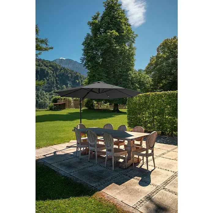 Sunfun Schirmbezug Capri - Anthrazit, Passend für: Sunfun Ampelschirmgestell Capri Ø 300 cm - Eine Gartenszene mit einem Esstisch und Stühlen unter einem großen Sonnenschirm, der Schatten spendet.