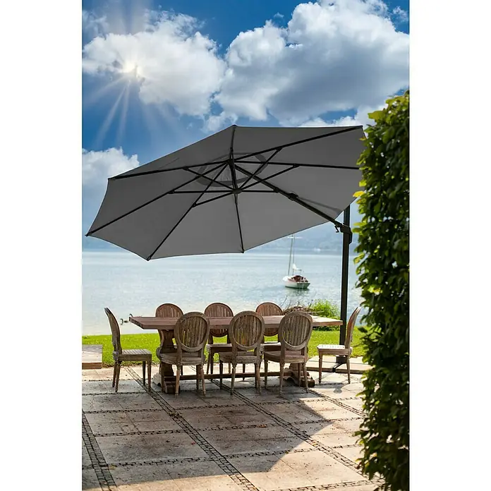 Sunfun Melina Schirmbezug - Anthrazit, Passend für: Sunfun Ampelschirmgestell Melina Ø 400 cm - Outdoor-Esstisch mit Sonnenschirm und Stühlen auf einer Terrasse mit Blick auf das Wasser.