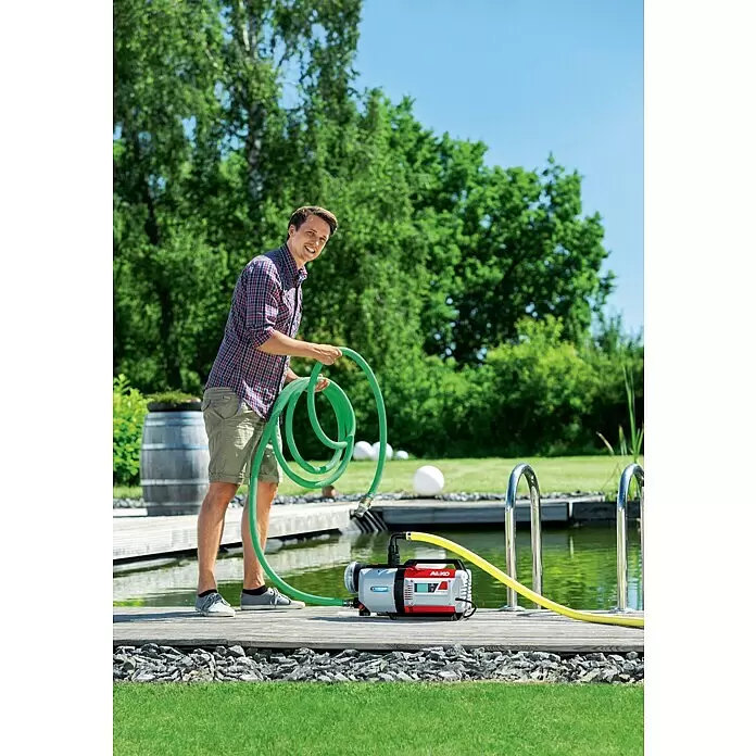 AL-KO Saugschlauchgarnitur - Länge: 7 m - AL-KO Pumpe (grau/rot) auf Holzdeck, zur Teichwasserübertragung mit Schläuchen, Mann mit grünem Schlauch.