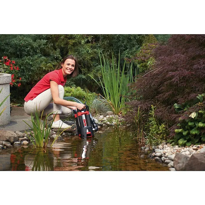 AL-KO Comfort Schmutzwasserpumpe Drain 15000 Inox - 1.100 W, Max. Fördermenge: 15.000 l/h, Eintauchtiefe: 7 m - Frau hockt am Teich und hält eine AL-KO Tauchpumpe in der Hand. Das Gerät ist ideal für Gartenteiche und sorgt für sauberes Wasser.