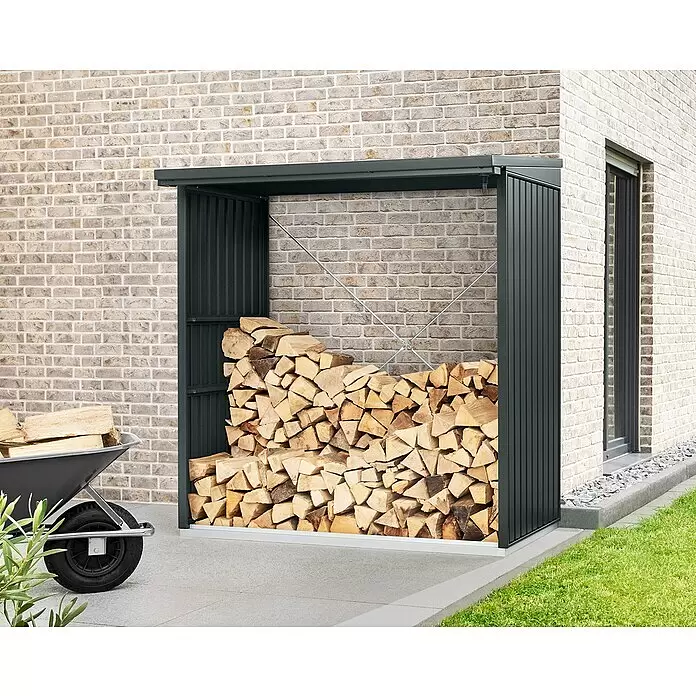 EcoStar Kaminholzregal Trend-V Typ 2 - Metall, Anthrazitgrau - Dunkelgraues Metall-Kaminholzregal, gefüllt mit gestapeltem Holz, steht im Freien an einer Ziegelwand, mit einer Schubkarre daneben.