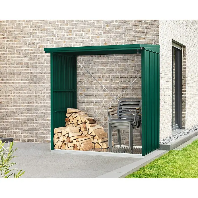 EcoStar Kaminholzregal Trend-V Typ 2 - Metall, Moosgrün - Ein grünes Brennholzlager mit Holz und Stühlen an einer Backsteinmauer bietet stilvolle und praktische Aufbewahrung im Außenbereich.