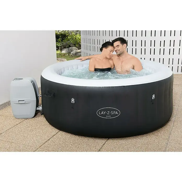 Bestway Lay-Z-Spa Mobil-Whirlpool Miami Air-Jet - Ø x H: 180 x 66 cm, Schwarz, 669 l - Ein Lay-Z-Spa Miami auf einer Terrasse mit einem Paar im warmen Wasser.