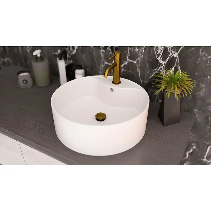 IO Válvula click clack - 1¼'', Oro - Primer plano de un baño moderno con lavabo redondo, grifo dorado y elementos decorativos sobre una pared de mármol.
