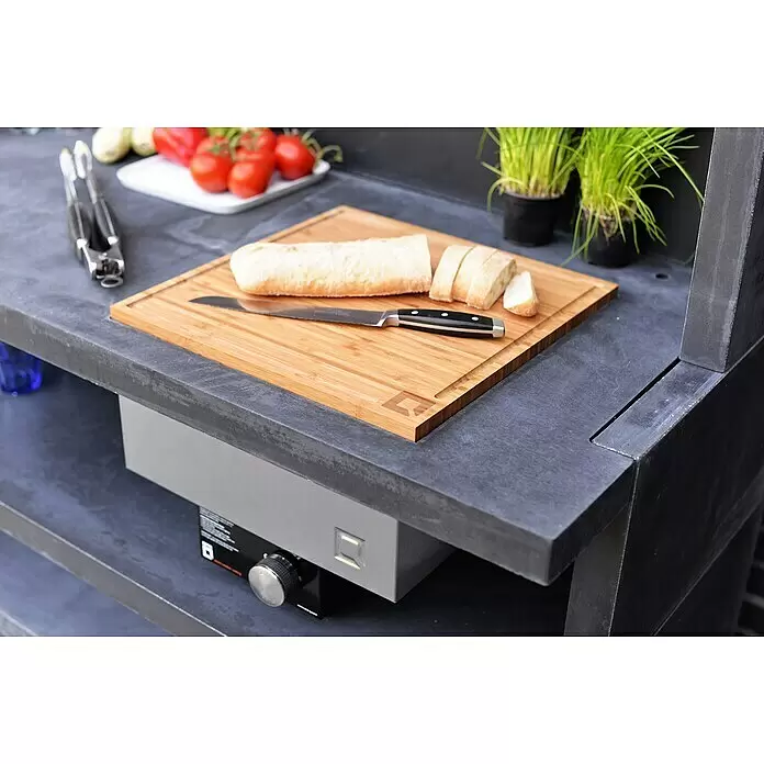 oneQ Schneidebrett - Bambus, L x B: 40,7 x 40,7 cm - Outdoor-Küche mit dunkelgrauer Arbeitsplatte, integriertem Brenner und Schneidebrett mit Brot, Messer und frischem Gemüse zur Zubereitung.