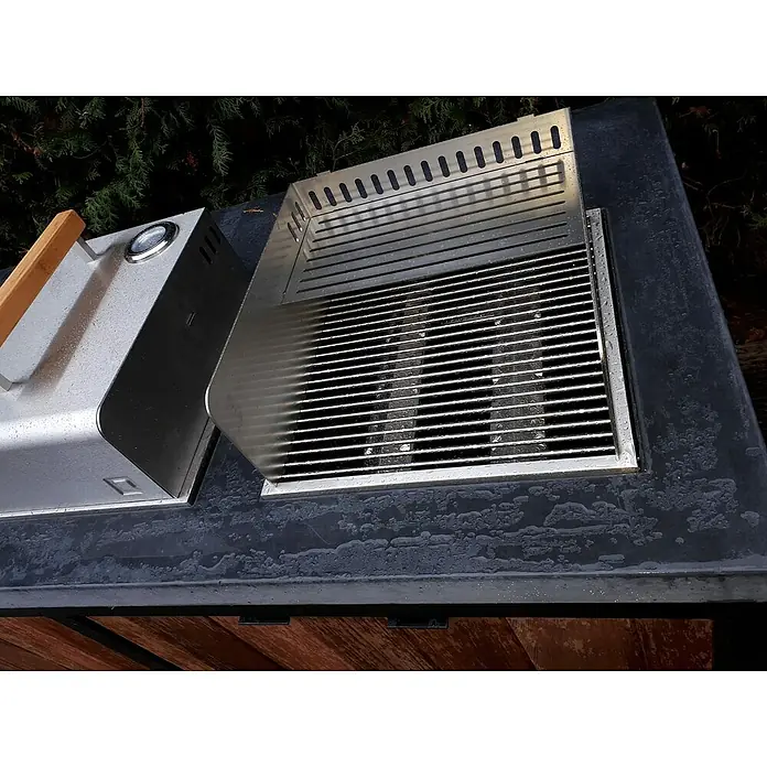 oneQ Grill-Schutzhülle mit Windschutz und Warmhalterost - Passend für: oneQ Holzkohlegrill Glow / oneQ Gasgrill Flame - Eine Nahaufnahme eines modernen Grills mit Grillrost und einem Seitenteil, beides aus glänzendem Metall, auf einer dunklen Arbeitsfläche.