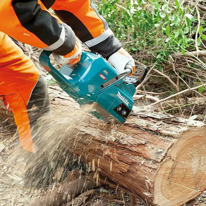 Makita XGT 40V max. Akku-Kettensäge UC012GT101 - 40 V, 5 Ah, Li-Ionen, 1 Akku, Schwertlänge: 40 cm - Ein Arbeiter sägt mit einer Makita Akku-Kettensäge einen Baumstamm. Die Kettensäge ist blaugrün und die Späne fliegen beim Sägen.