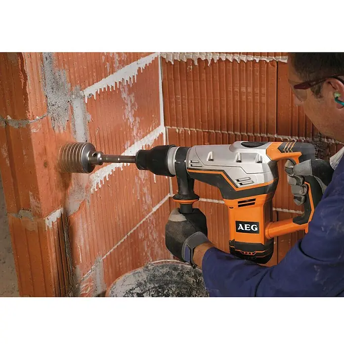 AEG Powertools Kombihammer KH 5 G - 1.100 W, 7,5 J, SDS-Max-Aufnahme - Ein AEG Bohrhammer wird benutzt, um ein Loch in eine Ziegelwand zu bohren. Der Bohrhammer ist orange und silber.