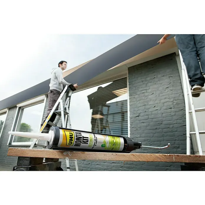 UHU Adhesivo para montaje Montakit Ultimate - 440 g, Cartucho - Adhesivo UHU Monta Kit sobre una mesa de madera con dos artesanos al fondo trabajando en escaleras en un edificio.