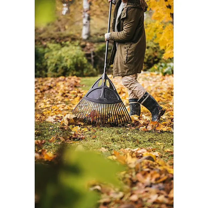 Fiskars Solid Laubbesen XL - Arbeitsbreite: 65 cm, Anzahl Zinken: 27, Langstiel - Eine Person im Garten harkt Blätter mit einem schwarzen Fiskars Laubbesen mit Teleskopstiel.