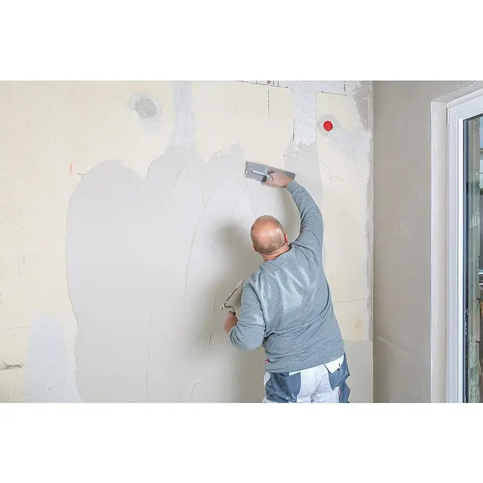 Knauf Rotband Flächenspachtel - 5 kg - Ein Handwerker glättet eine Wand mit einem Spachtel, um sie für die Endbearbeitung vorzubereiten. Die Spachtelmasse wird ebenmäßig aufgetragen.