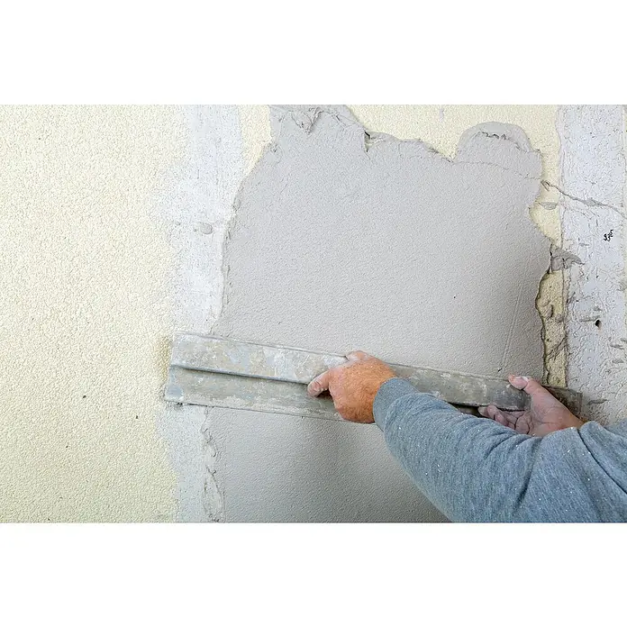 Knauf Rotband Flächenspachtel - 5 kg - Ein Handwerker glättet eine frisch verputzte Wand mit einem Spachtel, um eine ebene Oberfläche zu schaffen. Der Putz ist hellgrau, die Wand wird renoviert.
