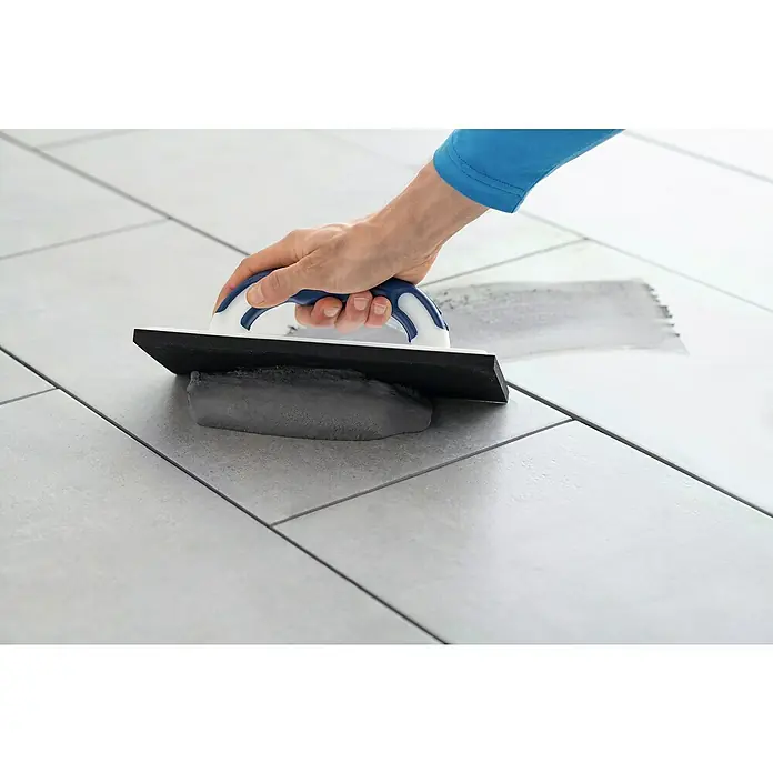 Knauf Flexfuge Universal - Manhattan, 10 kg - Ein Arbeiter verfugt mit einem Fugengummi graue Fliesen, um ein ebenmäßiges und sauberes Erscheinungsbild zu erzielen.