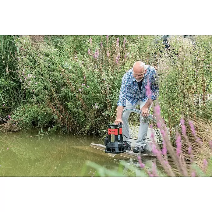 AL-KO Premium Schmutzwasserpumpe Drain 20000 HD - 1.300 W, Max. Fördermenge: 20.000 l/h, Eintauchtiefe: 7 m - Mann bedient eine rot-schwarze Tauchpumpe, um Wasser aus einem Teich zu pumpen.