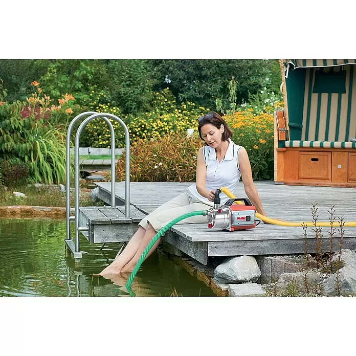 AL-KO Classic Gartenpumpe Jet 3000 Inox - 650 W, Max. Fördermenge: 3.100 l/h - Rote und silberne AL-KO JET 3000 Wasserpumpe mit grünem und gelbem Schlauch, die eine Frau zum Ziehen von Wasser aus einem Teich verwendet.