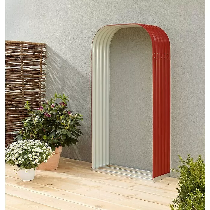 Vitavia Kaminholzregal Lignum 401 - 40 x 99 x 200 cm, Stahl, Rubin - Rot-heller Wellblechbogen steht auf einer Holzterrasse an einer strukturierten Wand, dient als dekoratives Gartenelement.