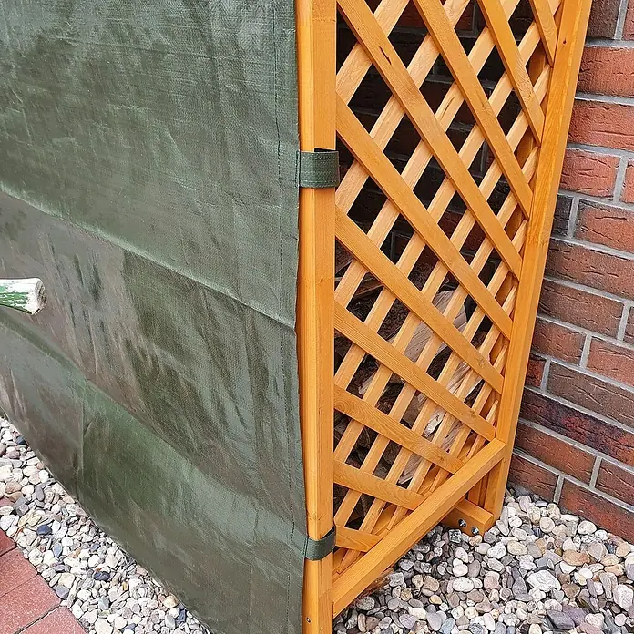 Promadino Kaminholzregal Speyer mit Wetterschutz - 120 x 68 x 148 cm, Honigbraun - Abdeckung aus Holz und Plane zum Schutz von Brennholz vor Witterungseinflüssen auf einem Kiesweg vor einer Ziegelmauer.