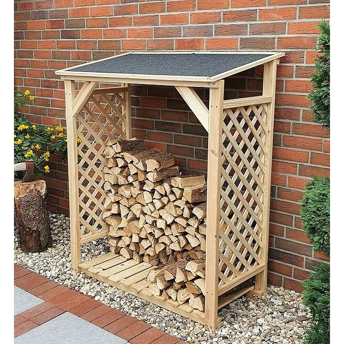 Promadino Kaminholzregal Speyer - 120 x 68 x 148 cm, Holz, Natur, Ohne Wetterschutz - Ein hölzerner Kaminholzunterstand mit Lattenrost an den Seiten, der Holzscheite lagert, steht an einer Ziegelmauer.