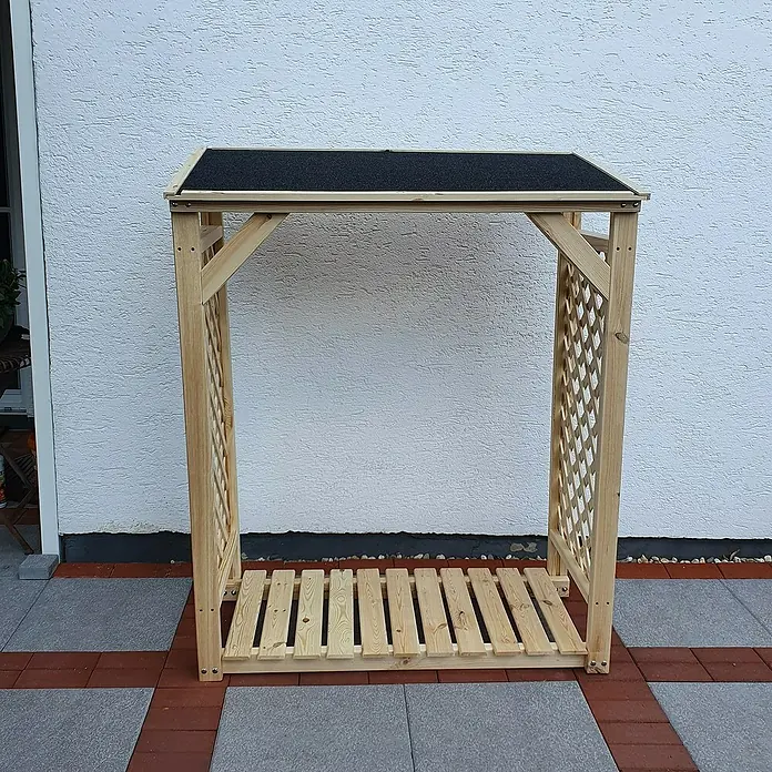 Promadino Kaminholzregal Speyer - 120 x 68 x 148 cm, Holz, Natur, Ohne Wetterschutz - Ein Holzlager mit Dach und Lattenstruktur steht auf einer gepflasterten Fläche vor einer weißen Wand. Praktisch und dekorativ für den Garten.
