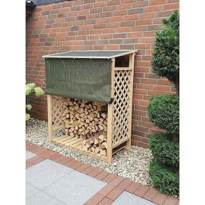 Promadino Kaminholzregal Speyer - 120 x 68 x 148 cm, Holz, Natur, Mit Wetterschutz - Brennholzregal aus Holz mit Abdeckplane, gefüllt mit Holzscheiten vor einer Backsteinmauer und einem Busch.