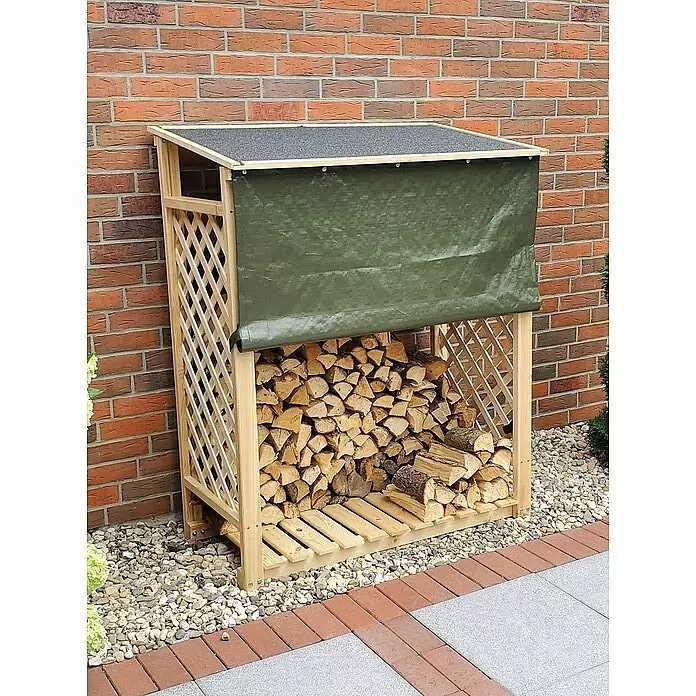 Promadino Kaminholzregal Speyer - 120 x 68 x 148 cm, Holz, Natur, Mit Wetterschutz - Ein heller Holzscheitlager mit dunklem Dach und grüner Plane, gefüllt mit Brennholz, steht vor einer Ziegelwand.