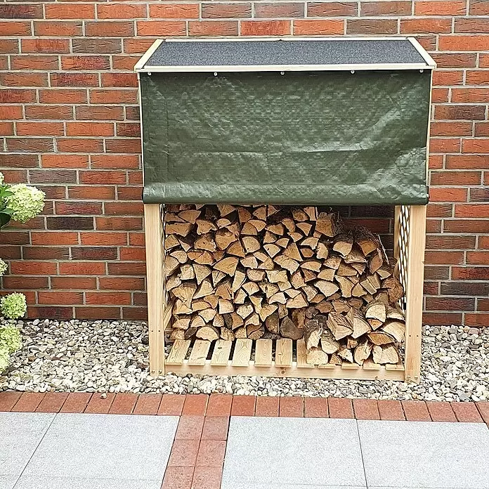 Promadino Kaminholzregal Speyer - 120 x 68 x 148 cm, Holz, Natur, Mit Wetterschutz - Holz-Lagerregal mit dunkelgrüner wasserdichter Abdeckung, gefüllt mit Brennholz, draußen an einer Ziegelwand platziert.