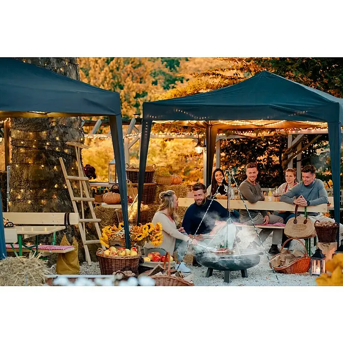 Buschbeck Schwenkgrill - Passend für: Buschbeck Feuerschale Ø 80 - 100 cm - Herbstliche Szene mit einer Gruppe von Personen, die sich um einen Grill versammelt haben, unter Zelten mit warmen Lichtern.