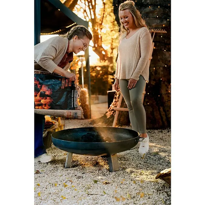 Feuerschale - Durchmesser: 80 cm, Eisen - Ein Außengrill wird mit Holzkohle befüllt, während zwei Frauen daneben stehen. Der Grill steht auf einem Kiesuntergrund.