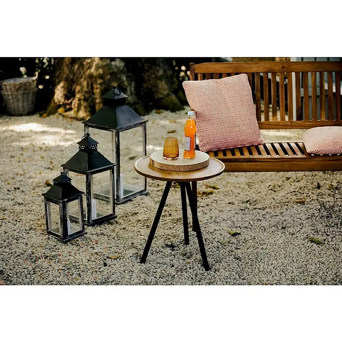 Sunfun Diana Gartenbank - B x T x H: 116 x 59 x 90 cm, Akazie, Naturbraun - Eine Szene im Freien mit Laternen, einem Getränk auf einem Tisch und einer Bank mit Kissen, die eine gemütliche Atmosphäre schaffen.