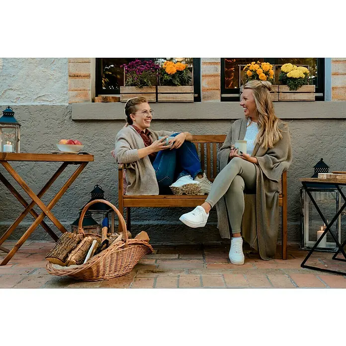 Sunfun Diana Gartenbank - B x T x H: 116 x 59 x 90 cm, Akazie, Naturbraun - Zwei Frauen sitzen auf einer Bank mit Strickjacken und trinken Kaffee, während sie eine gemütliche Atmosphäre genießen.
