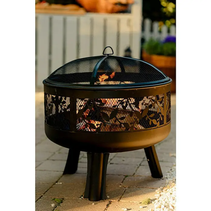 Buschbeck Feuerschale Leaves - Durchmesser: 63 cm, Stahl - Nahaufnahme einer schwarzen Feuerstelle mit Blattmuster und Gitter, die auf einer Terrasse für eine warme Atmosphäre sorgt.