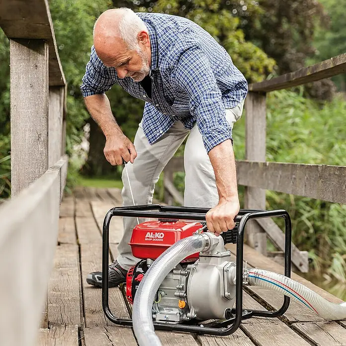 AL-KO Schmutzwasserpumpe - 4,1 kW, Max. Fördermenge: 30.000 l/h, Eintauchtiefe: 6 m - Ein Mann bedient eine AL-KO BMP 30000 Benzin-Wasserpumpe auf einer Holzbrücke, ideal für Gartenbewässerung und Entwässerungsarbeiten.