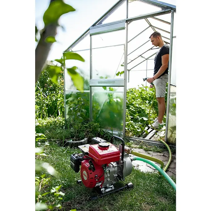 AL-KO Benzinwasserpumpe BMP 140011,7 kW, Max. Fördermenge: 12.000 l/h - Ein roter AL-KO Benzinwasserpumpe mit einem grünen Schlauch liegt vor einem Gewächshaus, in dem ein Mann Pflanzen bewässert.