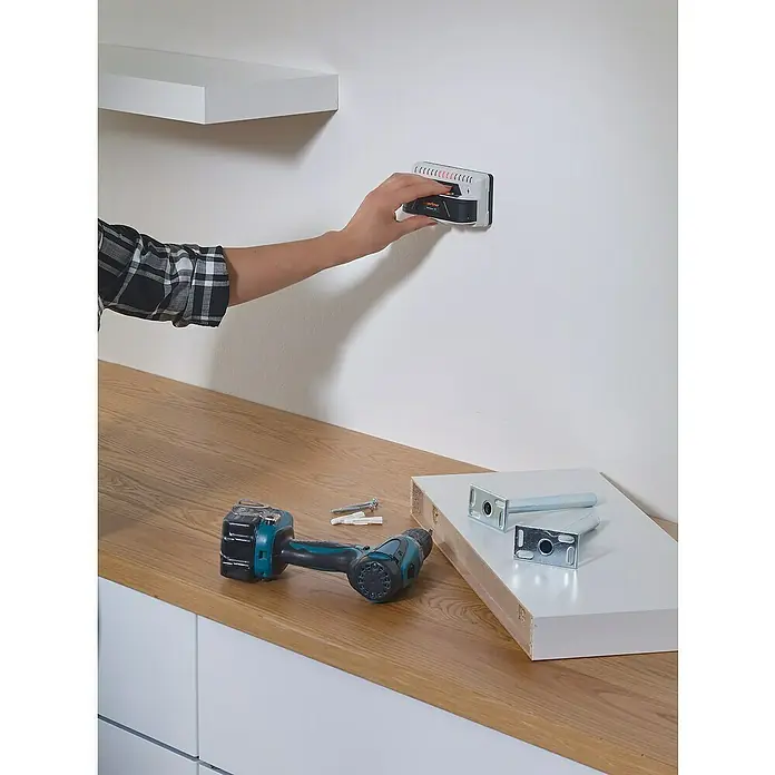 Laserliner Ortungsgerät StarSensor 150 - Geeignet für: Aufspüren von spannungsführenden Leitungen, Holz und Metall, Erfassungstiefe: Max. 40 mm Holz/Metall - Eine Person verwendet einen elektronischen Detektor, um eine Wand nach Bolzen abzusuchen, um Regale anzubringen. Schrauben und eine Bohrmaschine liegen bereit.