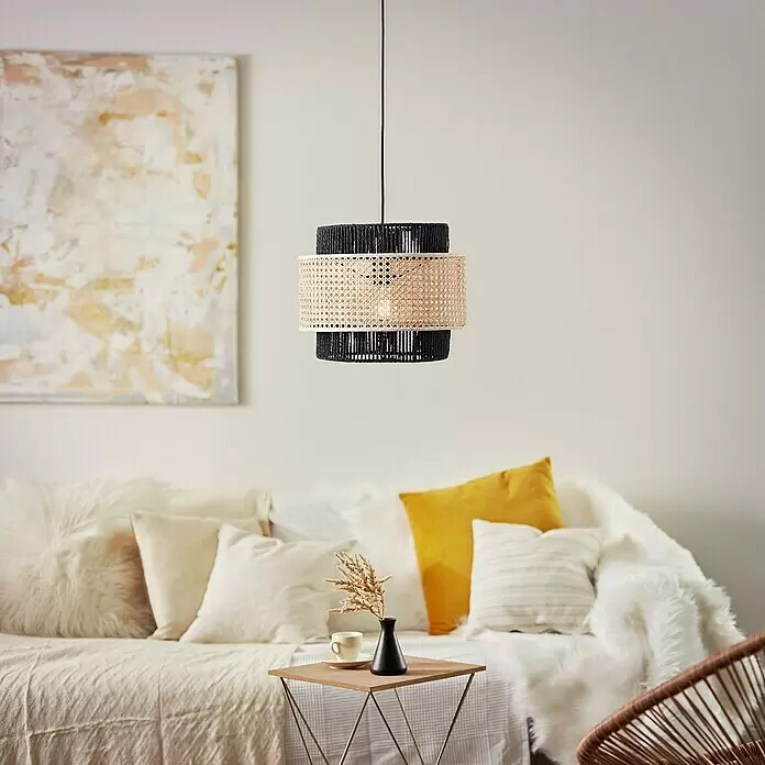 Brilliant Pendelleuchte Arles - 40 W, Schwarz, E27 - Pendelleuchte aus schwarzem und natürlichem Rattan, über einem Sofa in einem gemütlichen Wohnzimmer.