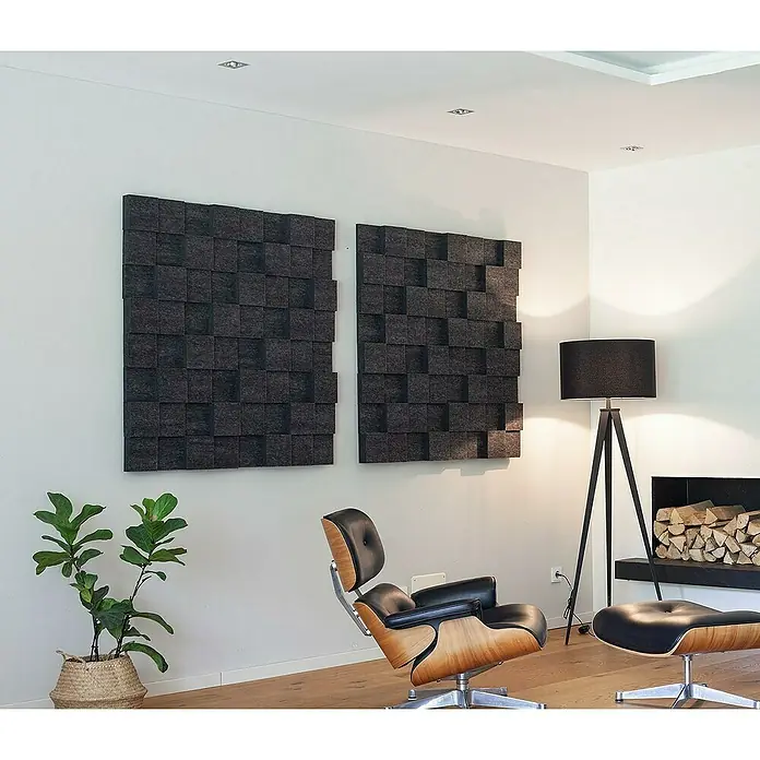 Silenti Akustikpaneel CubeLevel - Anthrazit, 100 cm x 50 cm x 80 mm, 100 % Polyester - Das Bild zeigt zwei graue, dekorative Akustikplatten an einer weißen Wand, die ein stilvolles Wohnzimmer ergänzen. Ein Sessel und eine Zimmerpflanze sind ebenfalls zu sehen.