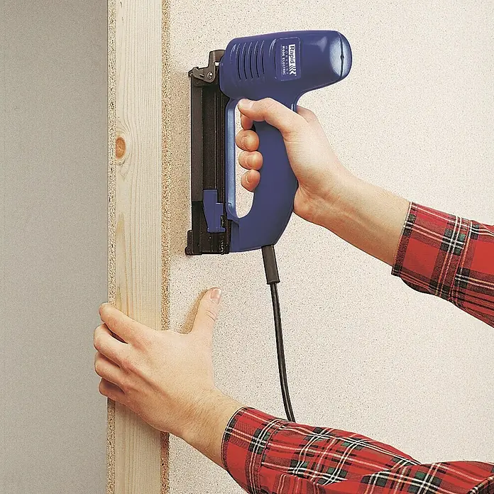 Rapid Elektrotacker R606 PRO - Klammertiefe: 12 mm - 25 mm, Geeignet für: Drahtstifte 15 - 25 mm, Verpackung: Schachtel - Eine Person befestigt ein Holzbrett mit einem blauen Rapid Elektrotacker an einer Wand.