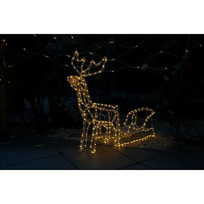 Tween Light LED-Lichtschlauch Rentier mit Schlitten - Anwendungsbereich: Außen, Warmweiß - Eine beleuchtete Rentier- und Schlittendekoration leuchtet nachts warm in einer Außenumgebung.