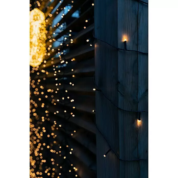Tween Light LED-Clusterlichterkette - Außen, Länge: 8,15 m, 768 Stk., Netzbetrieben, Lichtfarbe: Warmweiß - Warmweiße Lichterkette, die einen Holzpfosten beleuchtet und einen unscharfen dekorativen Hintergrund bildet.