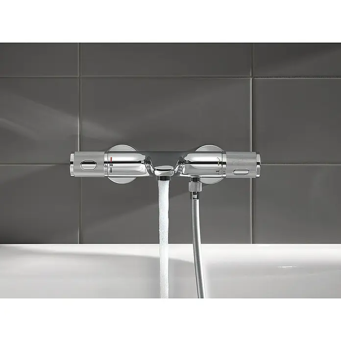 Grohe Precision Feel Wannenthermostat - Chrom, Glänzend - Ein chromfarbener Thermostat-Mischbatterie mit digitaler Temperaturanzeige und Brauseschlauch vor grauen Fliesen.